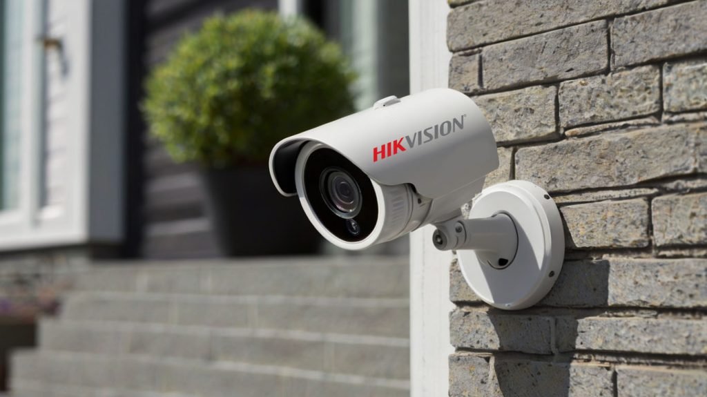 Cámara Hikvision en la pared con audio bidireccional instalada en la entrada de una casa, permitiendo comunicación a través de un teléfono móvil.